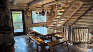 Ein rustikales Blockhaus-Interieur mit einem Holzesstisch, Bänken, einer Deckenleuchte und einer Treppe.