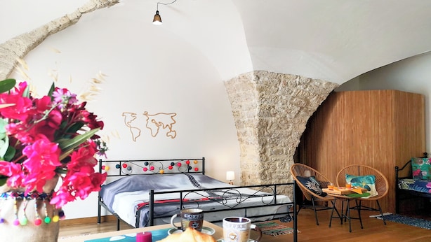 A cozy room with a bed, a dining table with pastries and coffee, a chair, and a decorative wall.