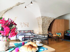 A cozy room with a bed, a dining table with pastries and coffee, a chair, and a decorative wall. - For old-Stones lovers (Poussan)