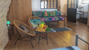 A cozy living area with a sofa adorned with colorful floral cushions, a wicker chair, and a small wooden table with a bottle and glasses.