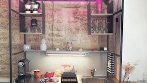 A compact kitchenette with a coffee machine, a sink, and a small refrigerator.