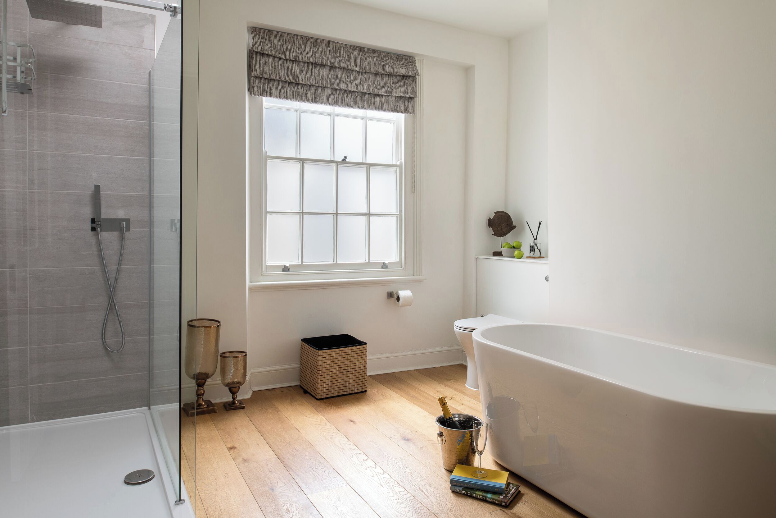 A modern bathroom with a glass shower enclosure, a freestanding bathtub, and a window with a valance.