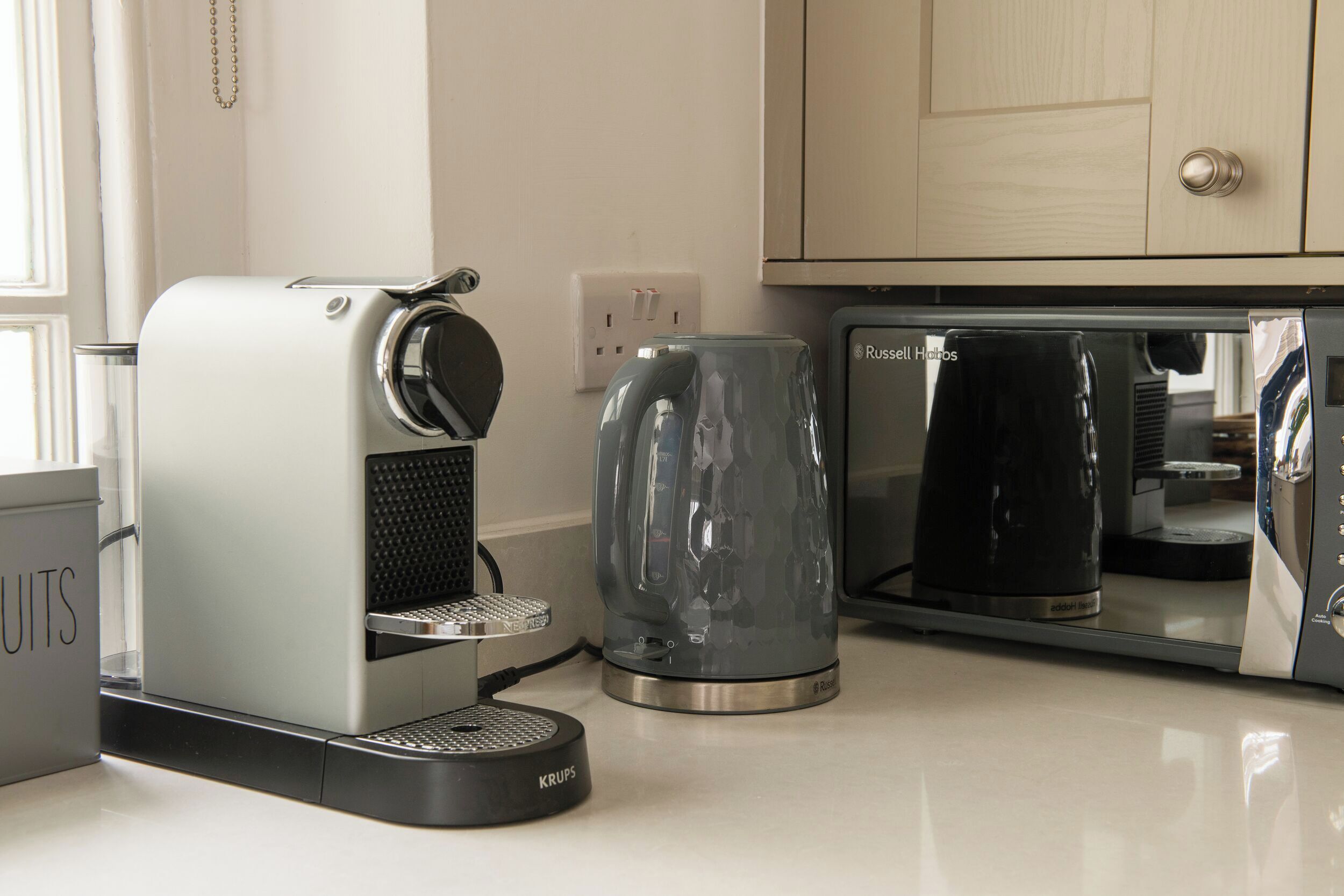 A kitchen with a coffee maker, a glass carafe, and a microwave.