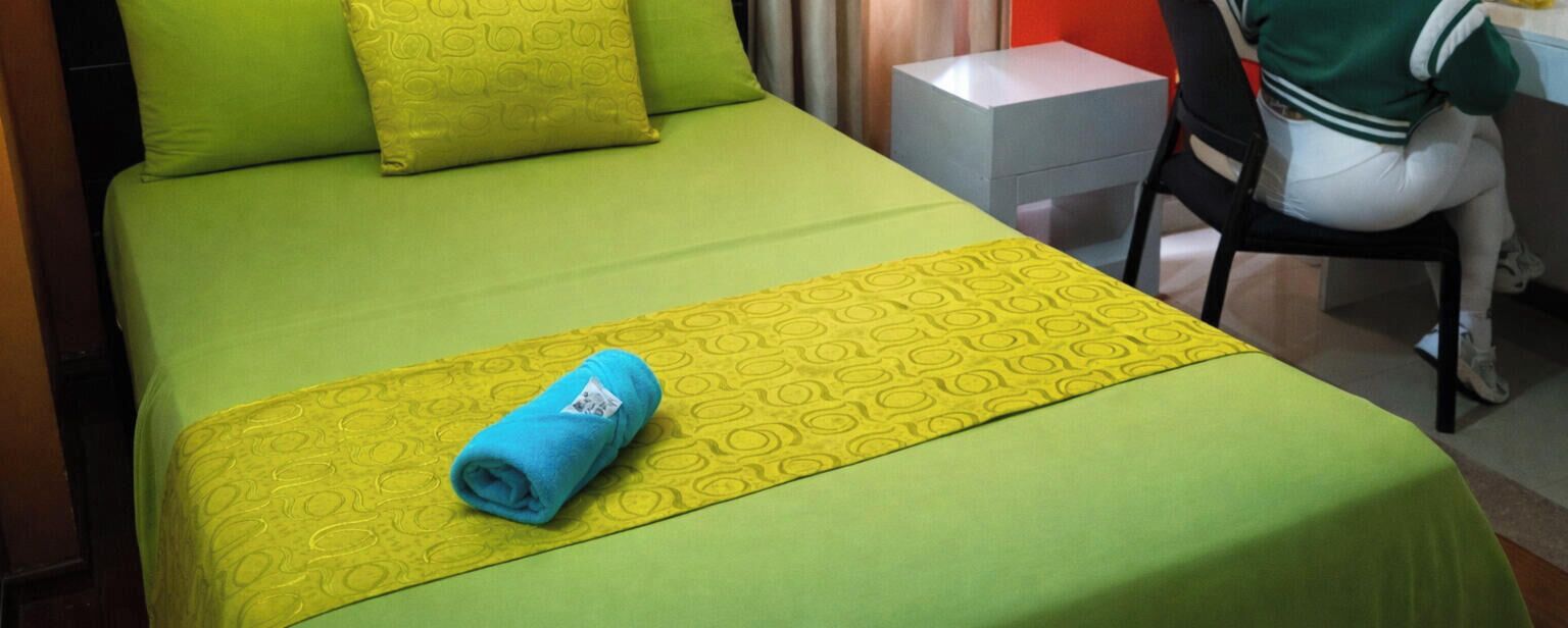 Una habitación de hotel con una colcha verde, un corredor de cama amarillo estampado y una toalla azul.