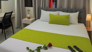 A hotel room with a bed, a desk, a chair, a nightstand, a lamp, a TV, and a window with curtains. - HOSTAL SABAOTH (Quito)