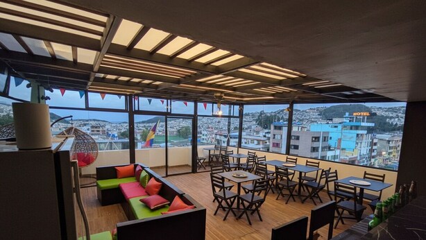 A rooftop dining area with tables and chairs, a sofa with colorful cushions, and a view of the cityscape. - HOSTAL SABAOTH (Quito)