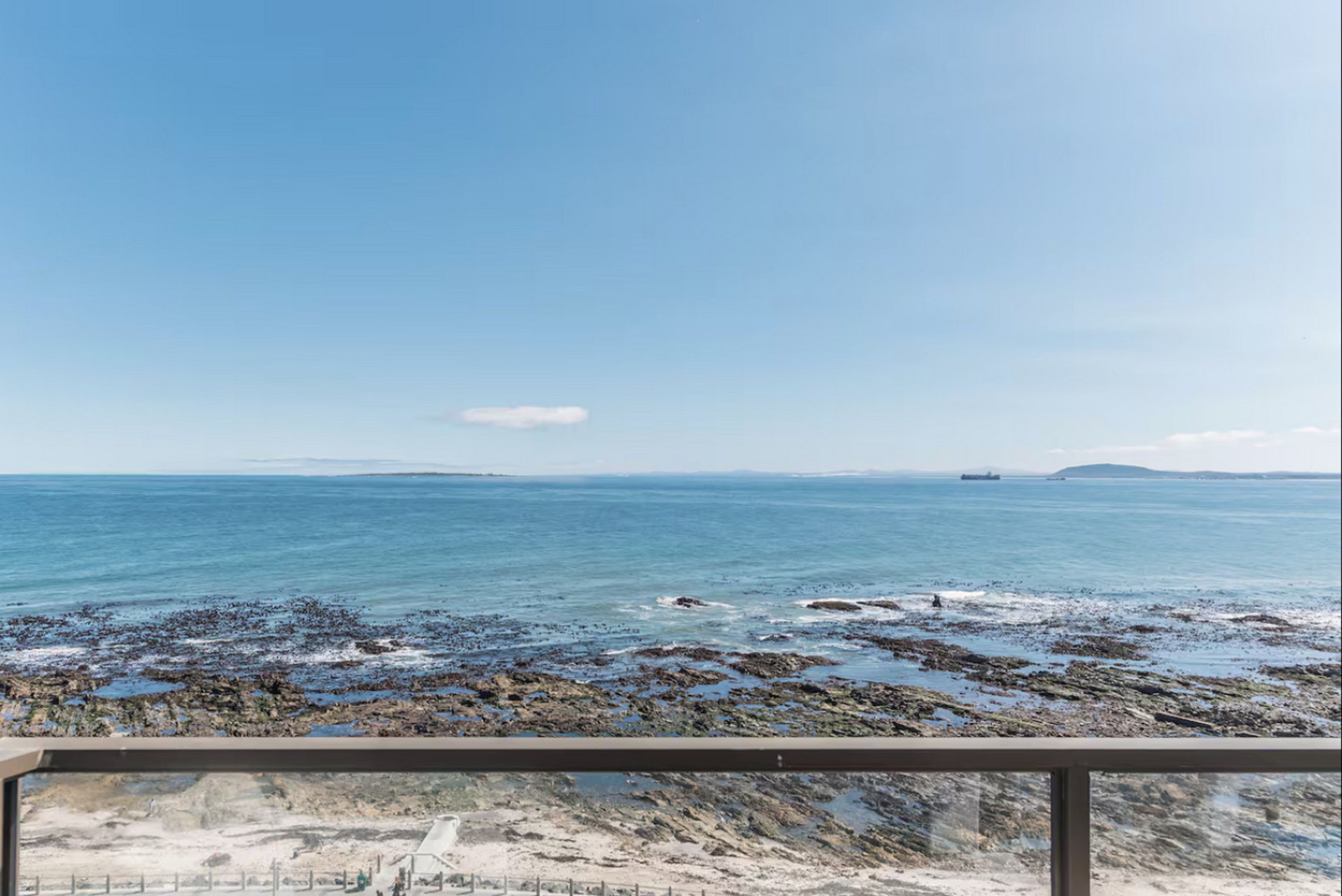 Blick auf die Küste vom Balkon aus, mit felsigem Ufer, einem Schiff in der Ferne und blauem Himmel.