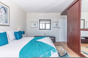 A bedroom with a bed, a wardrobe, a desk, and a window. - Secure One Bed | Uninterrupted Ocean Views (Cape Town)
