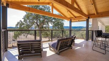 A covered outdoor seating area with two wooden benches, a metal grill, and a view of a tree and landscape.