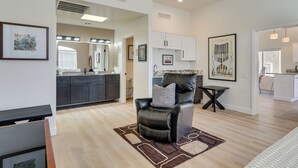A modern living room with a leather chair, a dining table, and a kitchen in the background.