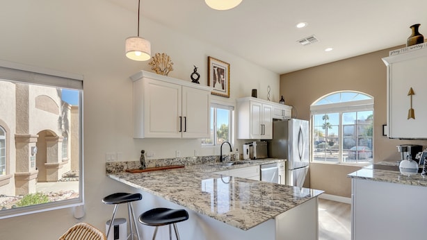 A modern kitchen with white cabinets, a granite countertop, and a large island with bar stools.