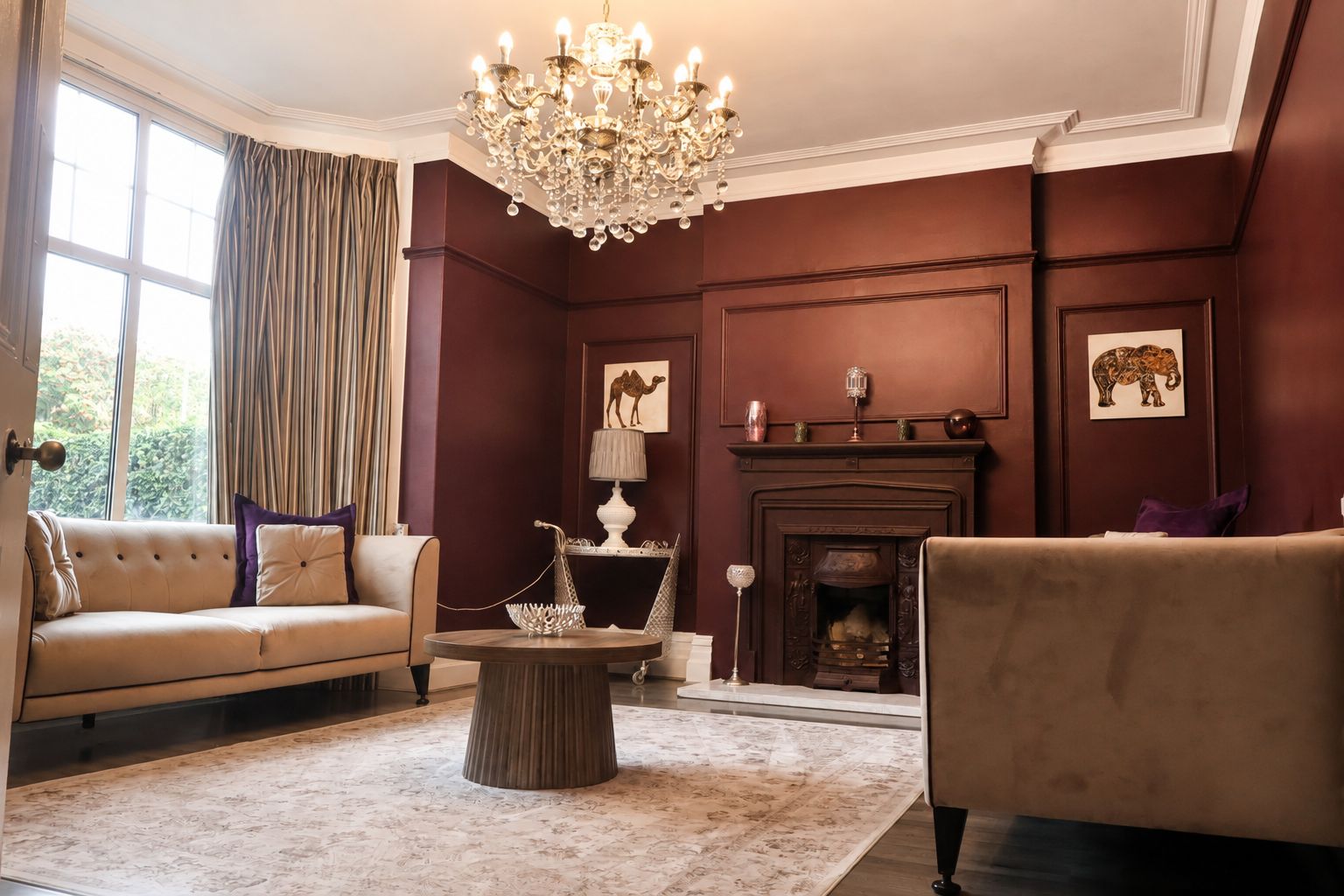 A room with a fireplace, a sofa, a chair, a chandelier, and a large window with curtains.