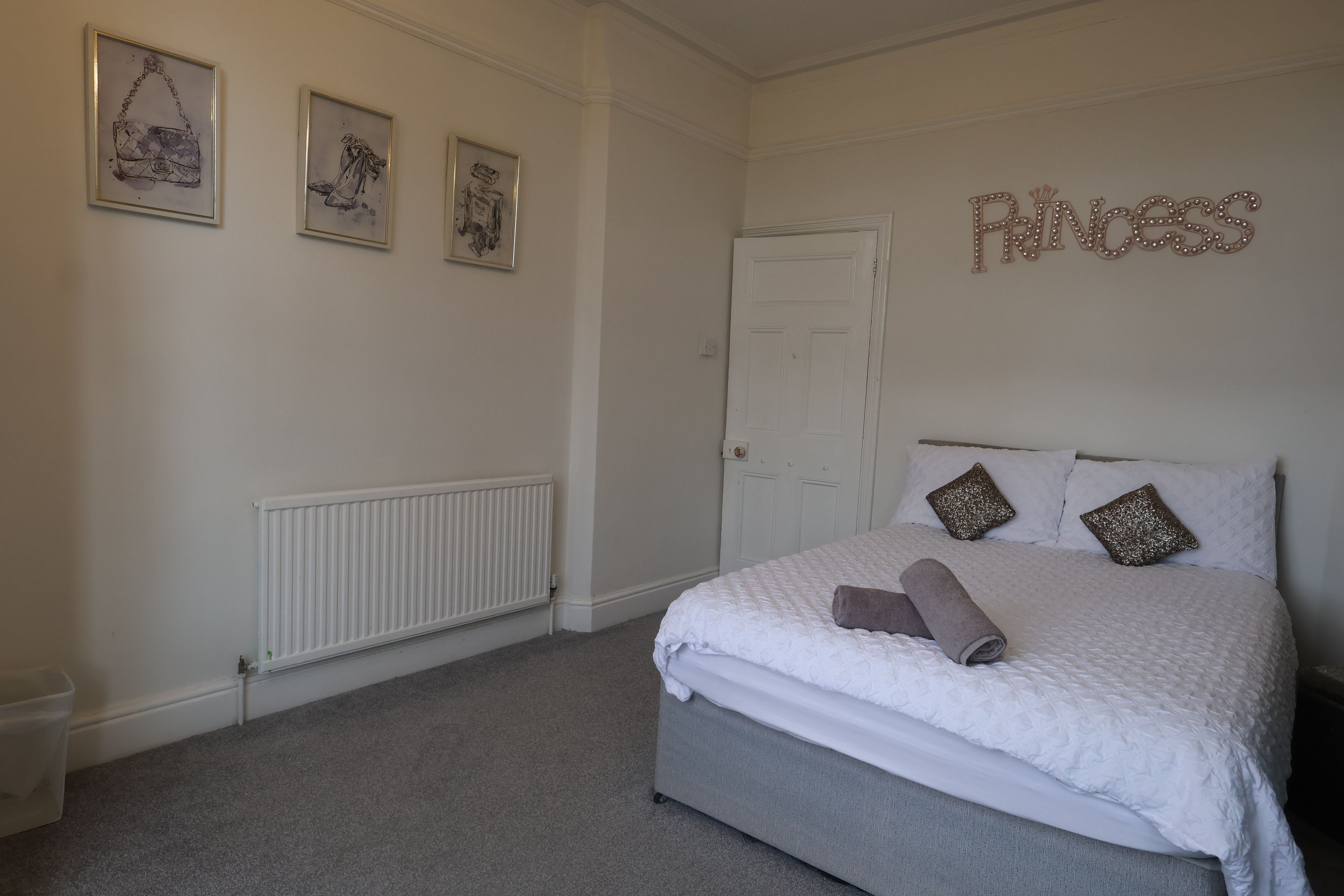 Une chambre à coucher avec un lit, un radiateur et trois œuvres d’art encadrées accrochées au mur.