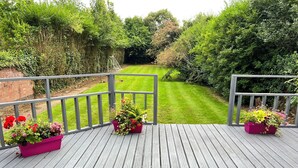 Um deck de madeira com vista para um gramado e jardim bem cuidados.