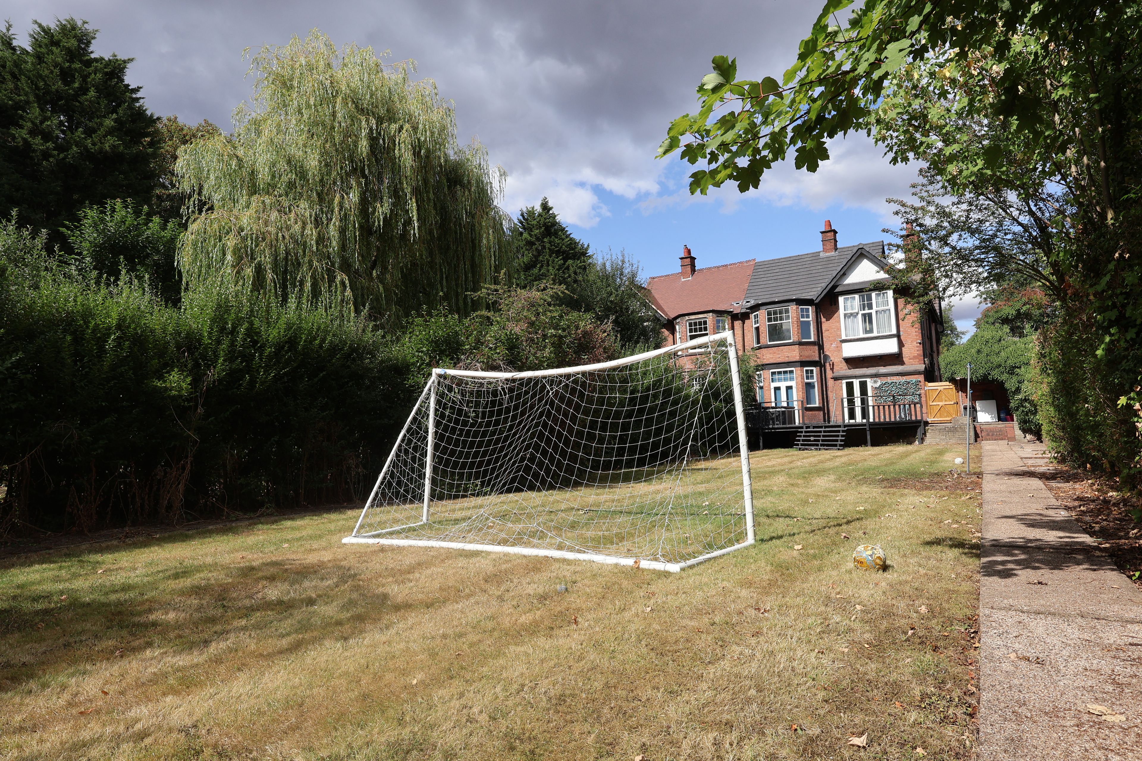 Un quartier résidentiel avec un terrain herbeux, un but de football et une maison en briques dotée d’une cheminée.