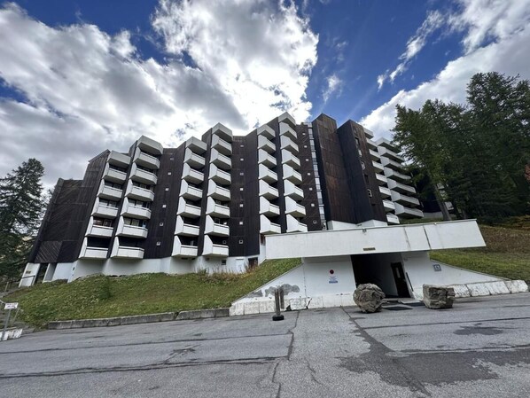 Un immeuble à plusieurs étages doté de balcons, d’un espace de stationnement et d’une pente herbeuse.