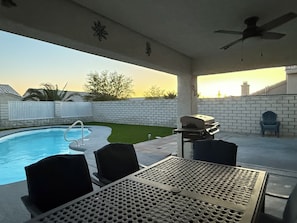 An outdoor patio with a pool, a grill, and a table with chairs.
