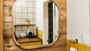 Interior de madera con un espejo redondo, una estantería con una planta, un hervidor y un perchero para toallas.