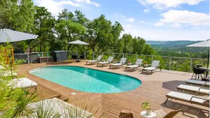 Una piscina con sillas de descanso y sombrillas, rodeada de vegetación y una vista panorámica.
