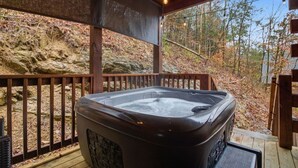 A hot tub on a wooden deck with a view of a rocky hillside and trees. - Cozy Cardinal with Hot Tub (Sevierville)