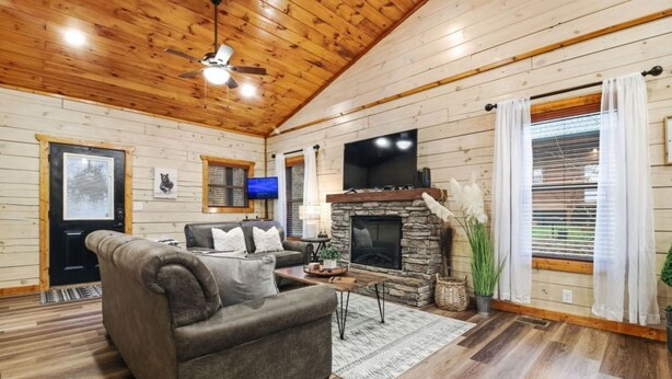 A cozy cabin interior with a stone fireplace, a sofa, a television, and a ceiling fan. - Cozy Cardinal with Hot Tub (Sevierville)