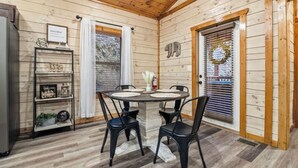 A wooden cabin interior with a round dining table, black chairs, a bookshelf, and a door with a wreath. - Cozy Cardinal with Hot Tub (Sevierville)