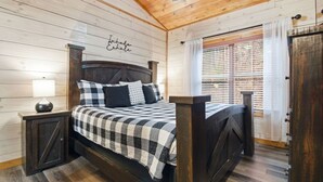 A wooden-paneled bedroom with a bed, a nightstand, a ceiling fan, and a window with blinds. - Cozy Cardinal with Hot Tub (Sevierville)