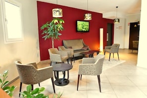 A modern living room with a red accent wall, a sofa, multiple armchairs, a coffee table, and a television. - Kyriad Chambery La Ravoire (La Ravoire)