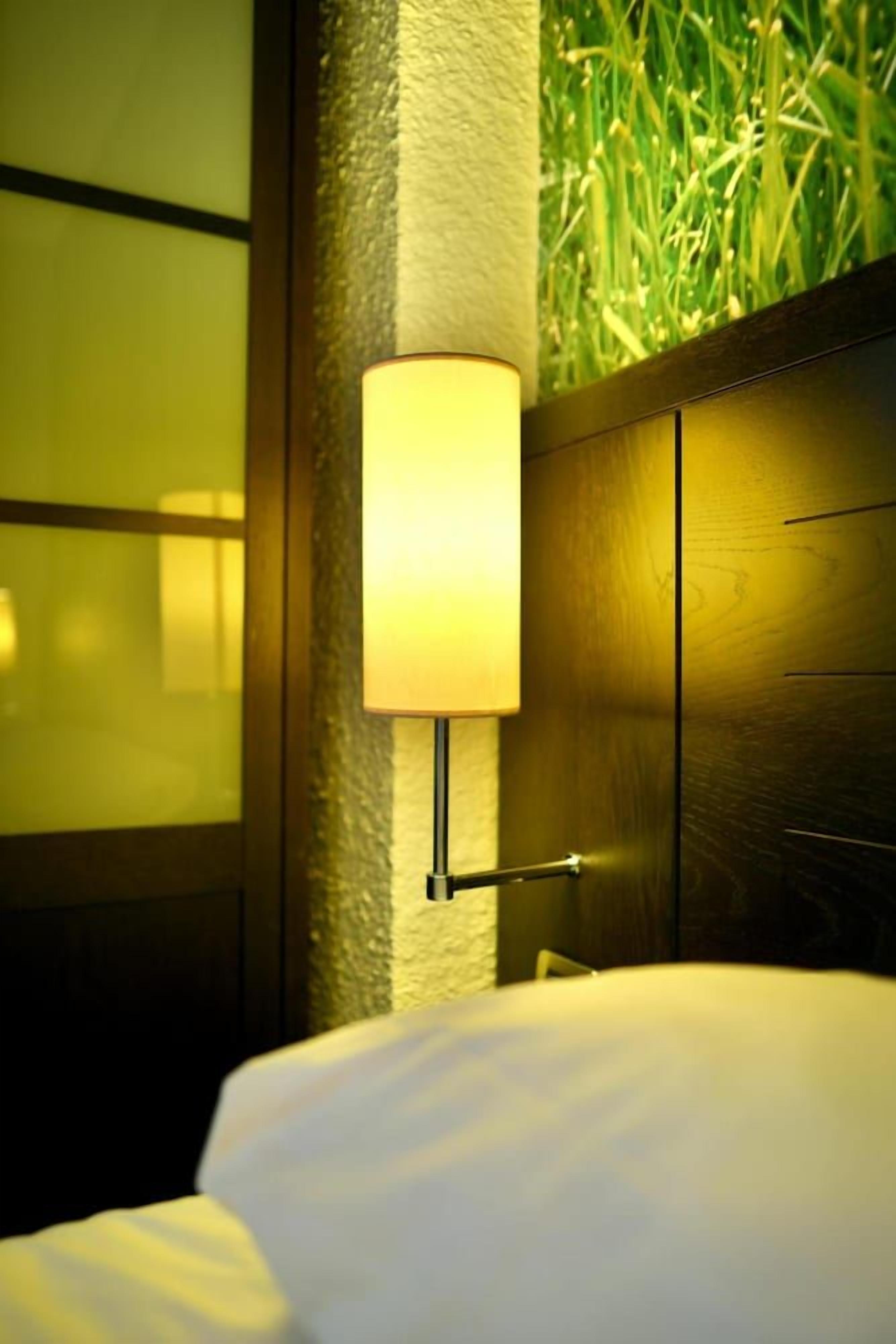 A hotel room with a bed, a wall-mounted lamp, and a textured wall.