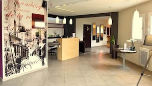 Um saguão moderno de hotel com balcão de recepção, um grande mural na parede e uma área de estar com mesa e cadeiras.