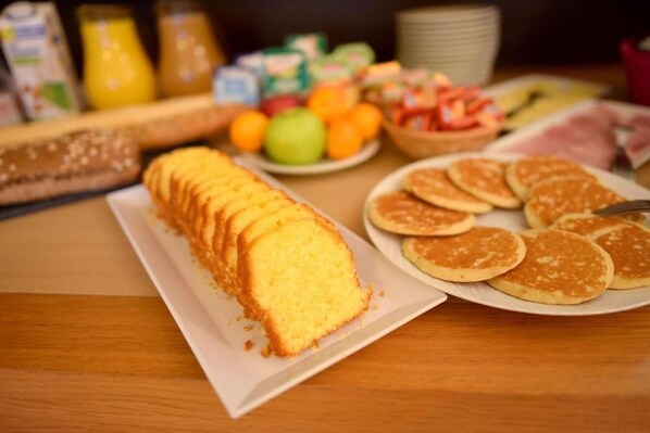 Une table de petit-déjeuner avec une miche de pain, des crêpes et un saladier de fruits.