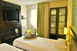 Une chambre d’hôtel avec un lit, une télévision, un plateau avec des articles pour le petit-déjeuner et une porte dont les panneaux sont en verre dépoli.
