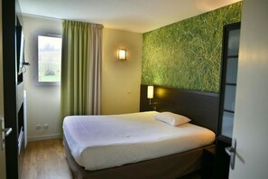 A hotel room with a bed, a window with curtains, a wall-mounted light, and a door. - Kyriad Chambery La Ravoire (La Ravoire)