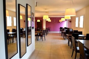A hotel dining area with multiple tables and chairs, large pendant lights, and a purple accent wall. - Kyriad Chambery La Ravoire (La Ravoire)