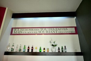 A wall with a sign in French, a shelf with various bottles, and a vase with flowers. - Kyriad Chambery La Ravoire (La Ravoire)