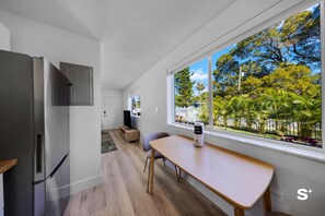 A modern kitchen with a built-in refrigerator, a dining area with a table and chairs, and a large window offering a view of a garden. - Cozy Miami 1-BD - Gym & Free Parking (North Miami)