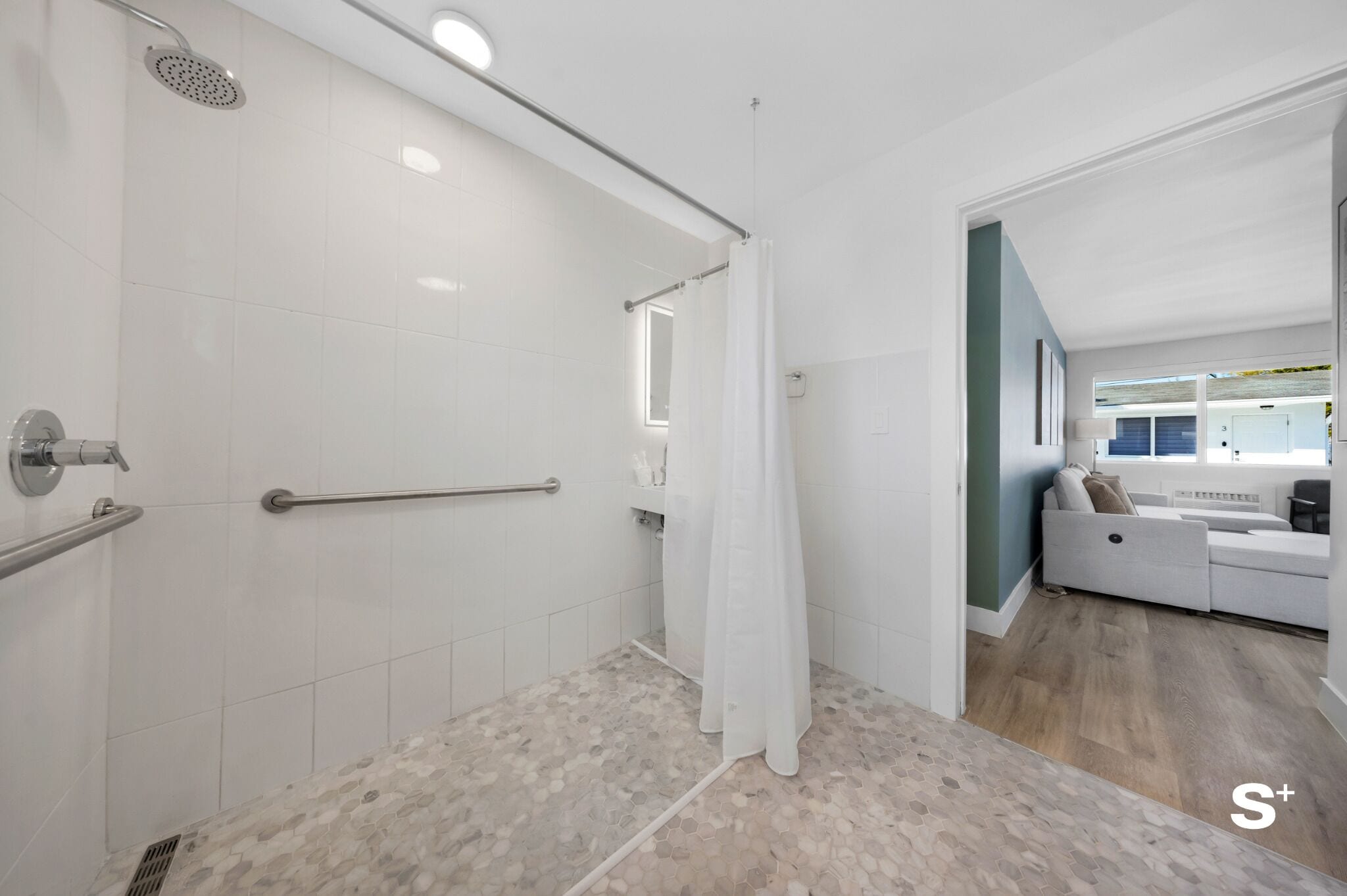 A modern bathroom with white tiles, a shower, a grab bar, and a visible towel rack.