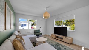 Een moderne woonkamer met een zithoek, een televisie en een groot raam met uitzicht op groen.