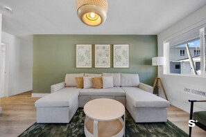 Un salon moderne avec un canapé d’angle, une table basse ronde et des reproductions botaniques encadrées accrochées au mur.