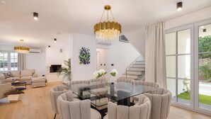 Een moderne woonkamer met een glazen eettafel, omringd door zes stoelen, een kroonluchter en een trap naar een ander niveau.