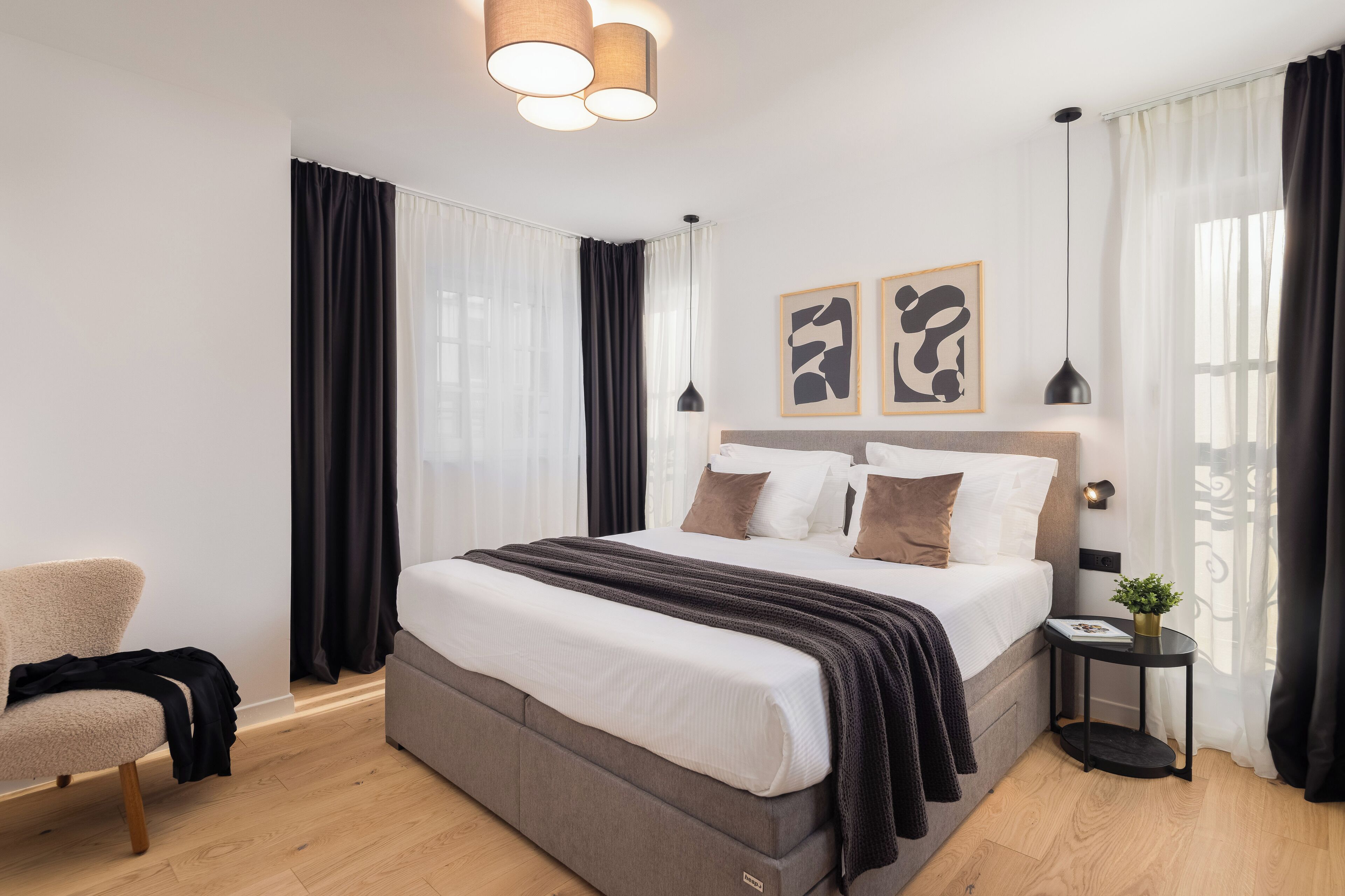 A modern bedroom with a large bed, a side table, a chair, and a window with curtains.