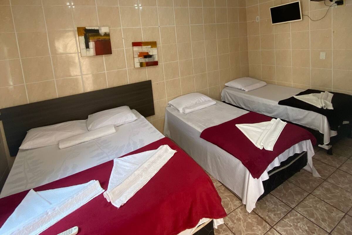 Habitación de hotel con tres camas, un televisor montado en la pared y una lámpara en el techo.