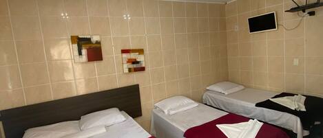 Habitación de hotel con tres camas, un televisor montado en la pared y una lámpara en el techo.
