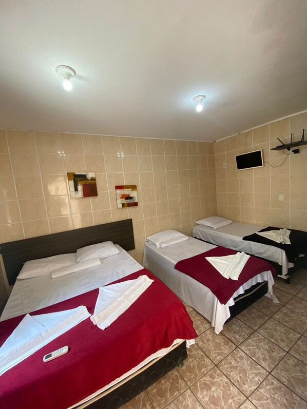 A hotel room with three beds, a TV mounted on the wall, and a ceiling light.