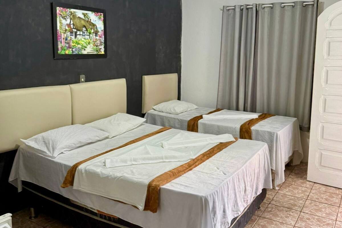Habitación de hotel con dos camas, una mesita pequeña, una silla, un cuadro en la pared y una cortina.