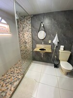 Um banheiro com chuveiro, pia, vaso sanitário e espelho.