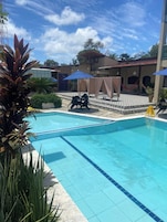 Piscina com deck ladrilhado, rodeada por plantas e guarda-sóis.