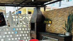 An outdoor kitchen area with a stone oven, a dining table with red chairs, and a tiled floor. - Novo Hotel Maracaipe (Ipojuca)