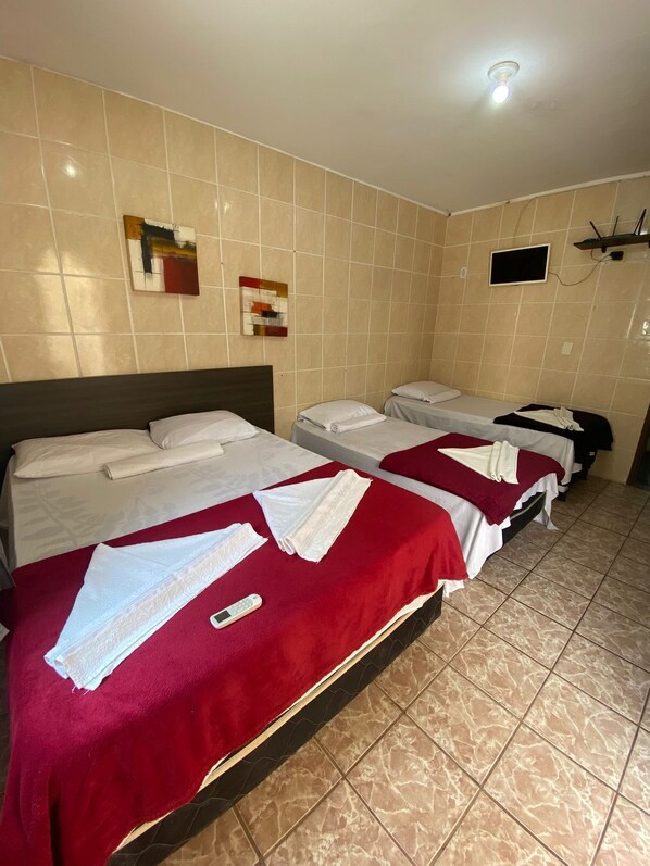 Habitación de hotel con dos camas, una manta roja, un reloj digital y un televisor pequeño en la pared.