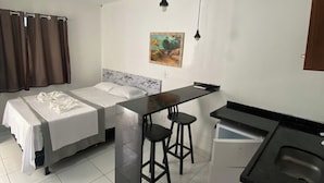 A compact hotel room with a bed, a small kitchenette, a dining area with stools, and a painting on the wall. - Novo Hotel Maracaipe (Ipojuca)